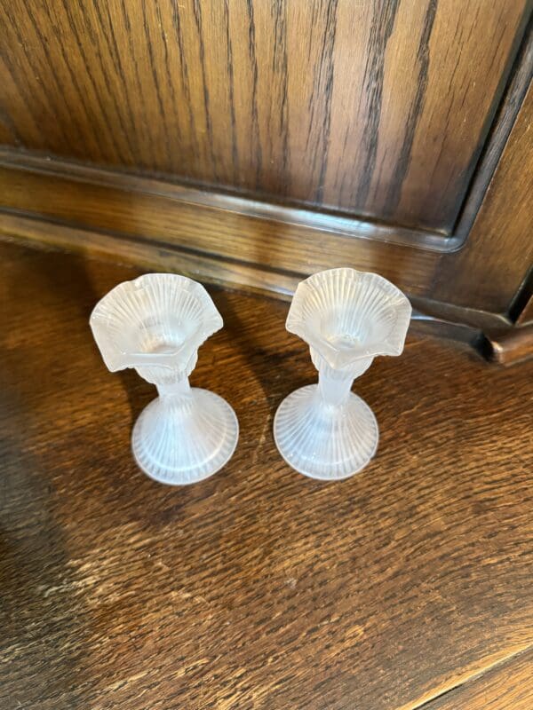 A pair of white glass candlesticks on top of a wooden table.