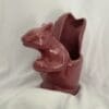 A red ceramic squirrel sitting on top of a vase.