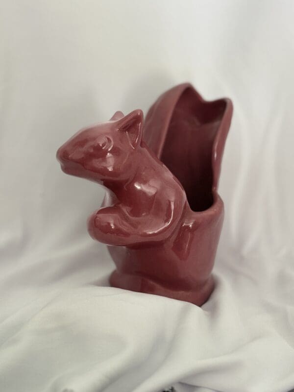 A red ceramic squirrel sitting on top of a vase.