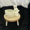 A small stool with a white ceramic pot on top of it.