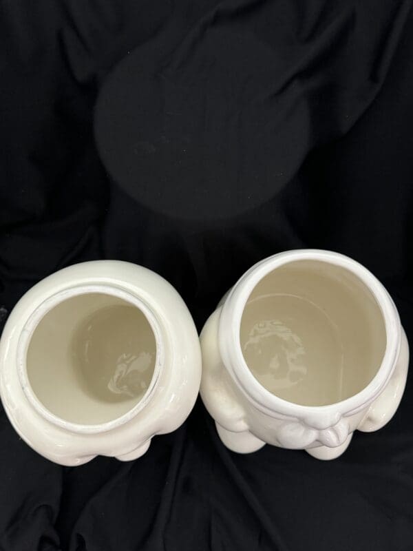 Two white vases sitting on top of a black cloth.