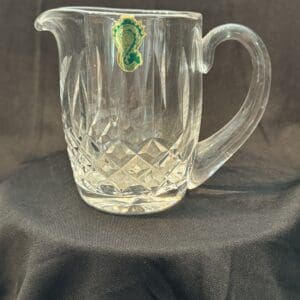 A glass pitcher with a green leaf on it.