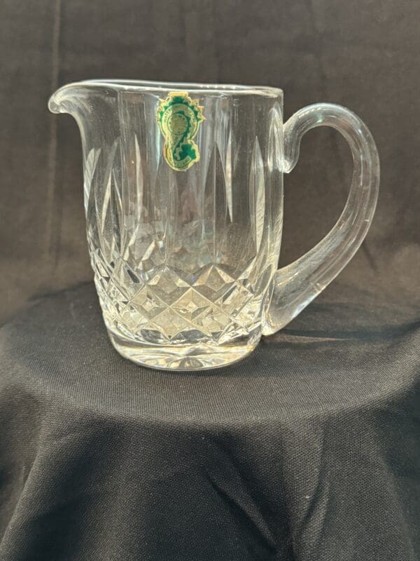 A glass pitcher with a green leaf on it.