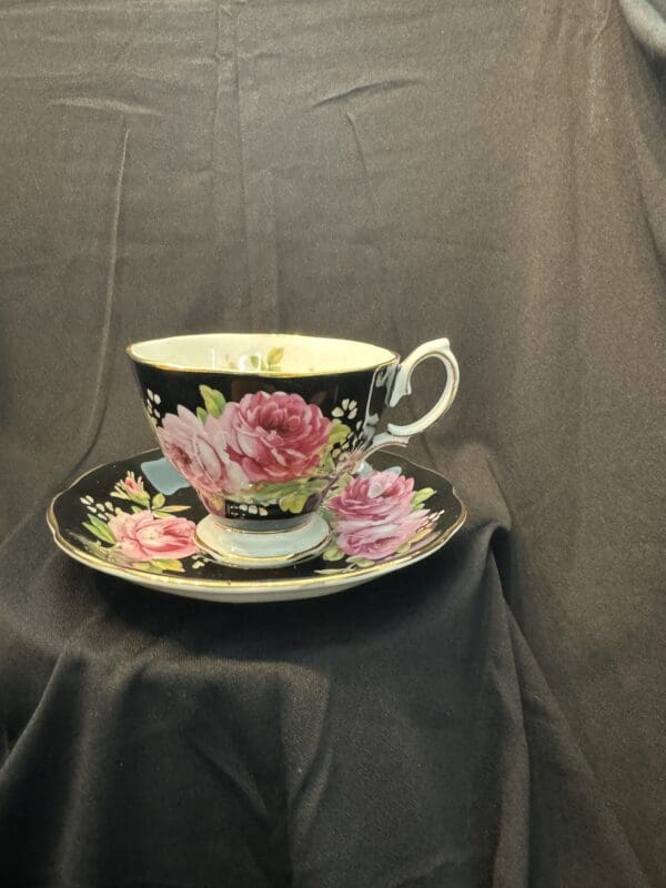 A black tea cup and saucer with pink flowers.