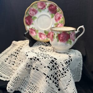 A tea cup and saucer on a table with a crocheted doily.