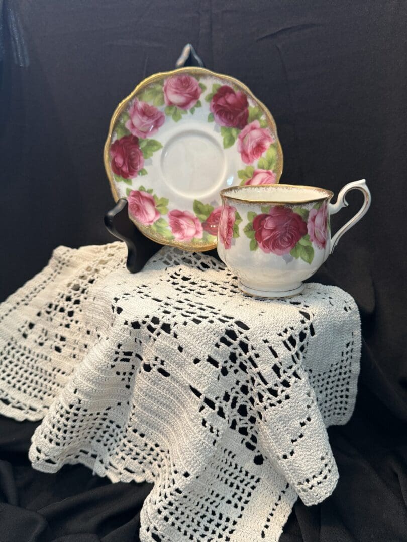 A tea cup and saucer on a table with a crocheted doily.