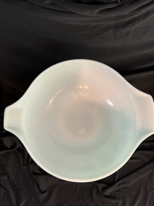 A white bowl with handles on top of black cloth.