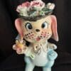 A ceramic dog with flowers on top of it's head.