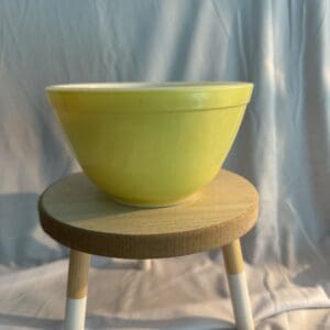 A yellow bowl sitting on top of a wooden stool.