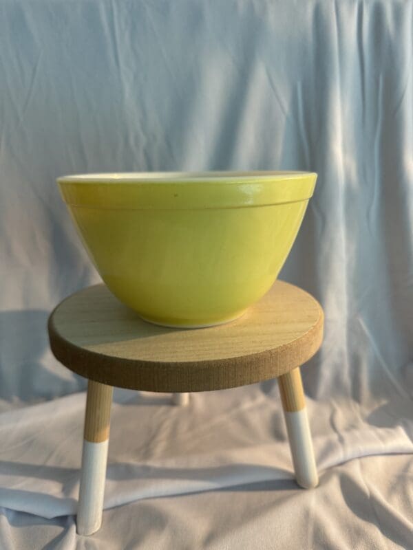 A yellow bowl sitting on top of a wooden stool.