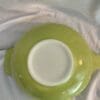 A green bowl with white rim on top of a bed.