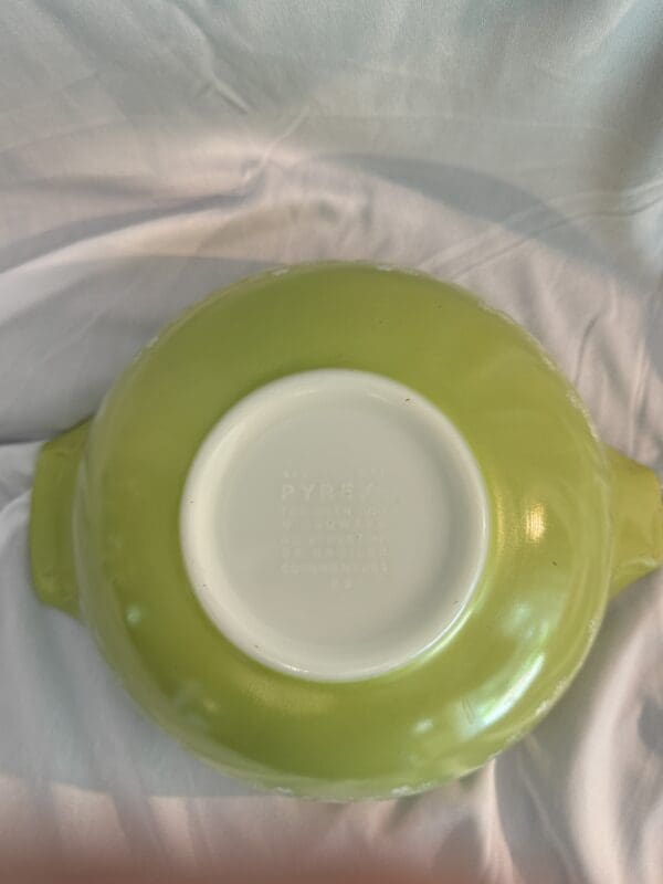 A green bowl with white rim on top of a bed.