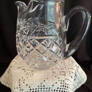A glass pitcher sitting on top of a crocheted doily.
