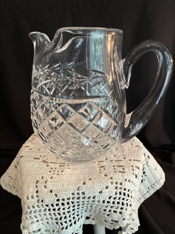 A glass pitcher sitting on top of a crocheted doily.