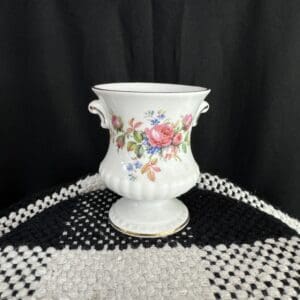 A white vase with flowers on it sitting on top of a table.