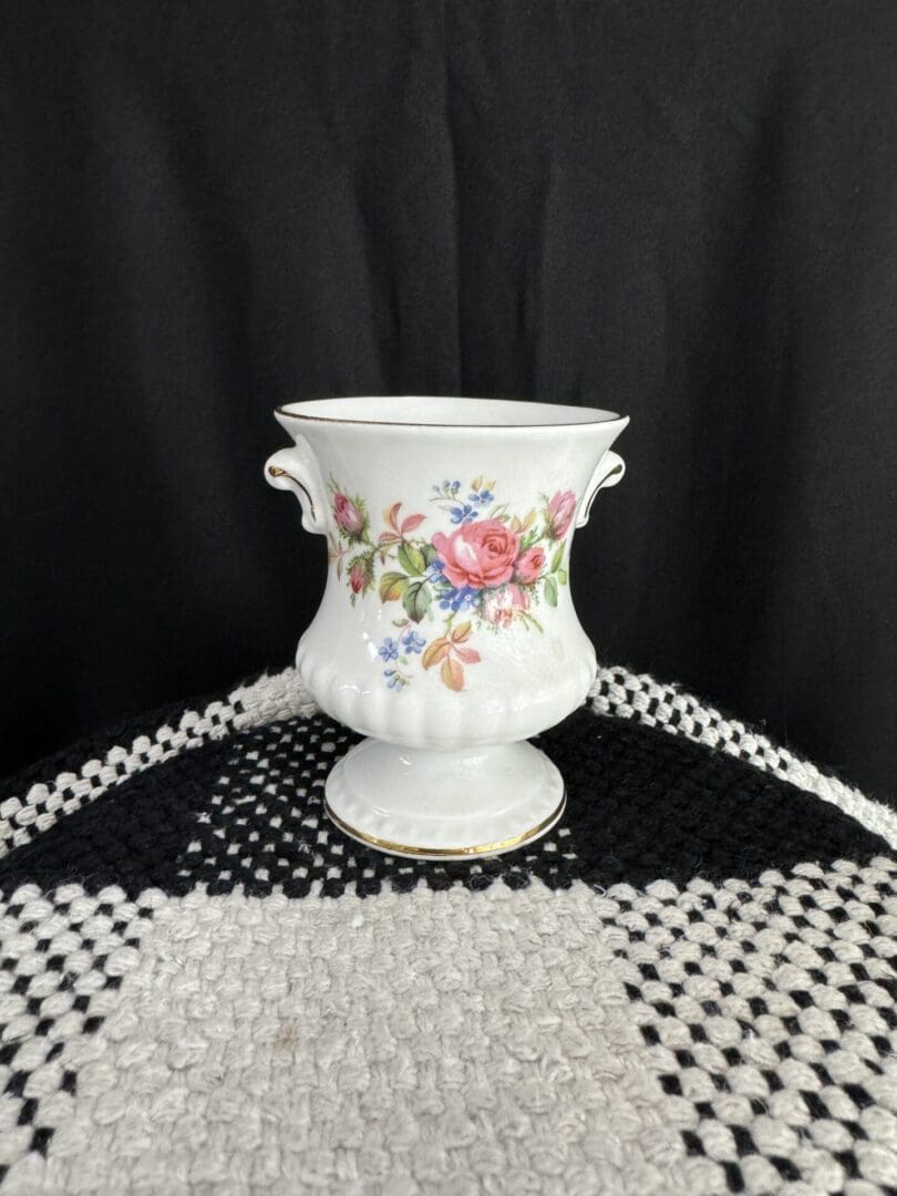 A white vase with flowers on it sitting on top of a table.