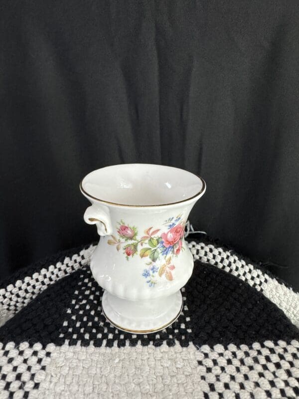 A white vase with flowers on top of a black table.