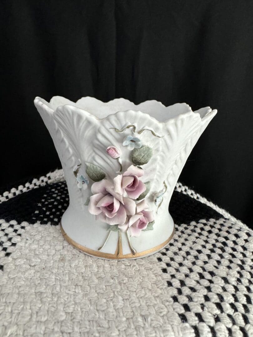 A white vase with pink flowers on top of a table.